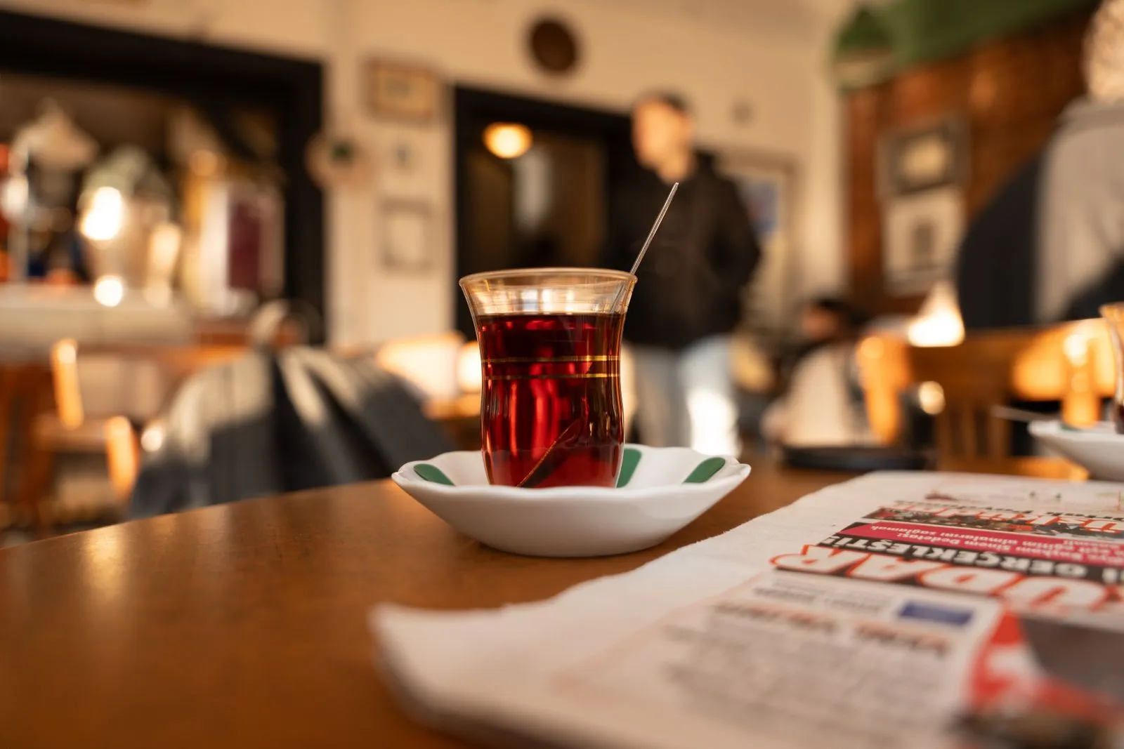 Warm cafe ambiance with Turkish tea and newspaper on table, blurred background.